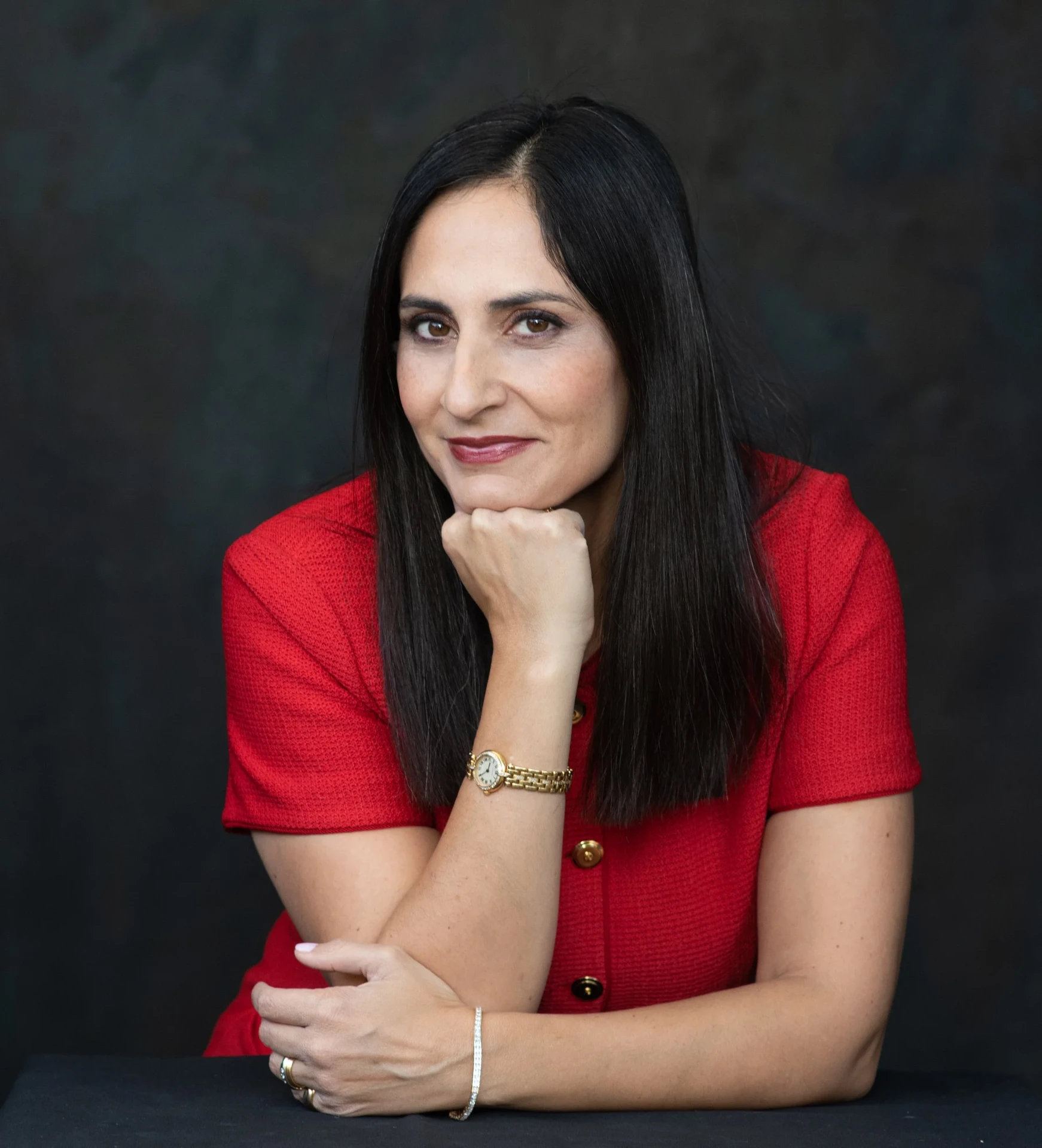 Pardis Mahdavi in a red dress, seated with her chin resting on her hand.